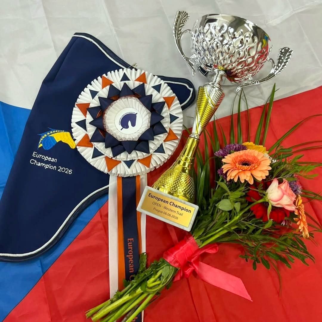 Ceny pro vítěze – tmavě modrá kokarda s nápisem European Champion 2026, zlatý pohár pro vítěze třídy Open Western Trail a kytice na pozadí české vlajky.